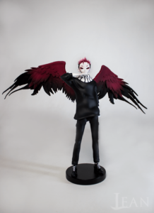 3D printed figure of an angel. The design belongs to SkullwalkerX. The figure wears only black clothes and has big wings in red and black. In addition, there is a very pale skin.